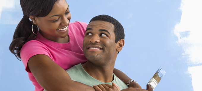 Black couple painting house wall.